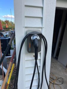 A black electric car charger attached to the side of a house.